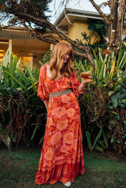 Rada Priya Campbell, fashion designer and entrepreneur wearing Nine Lives Bazaar at their collection launch for locomotion. The dress is long and flowing with hues of pink and red. She is holding a chilli margarita by Azteca