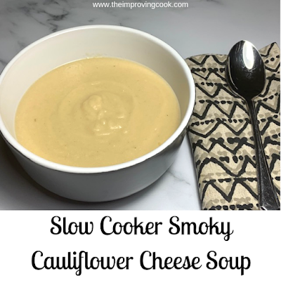 cauliflower soup in a grey bowl on a marble countertop with a patterned tea towel and a soup spoon