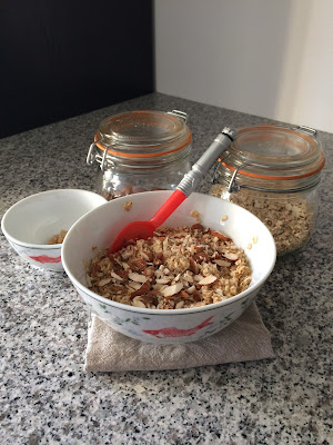 Un bol de flocons d'avoines aux amandes accompagné de deux bocaux en verre avec les ingrédients amande et flocons d'avoine sur plan de travail en granit