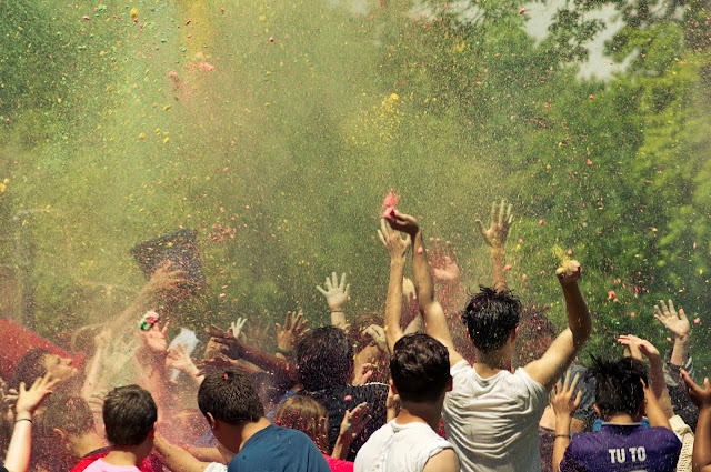 People jump and throw color in air with trees around