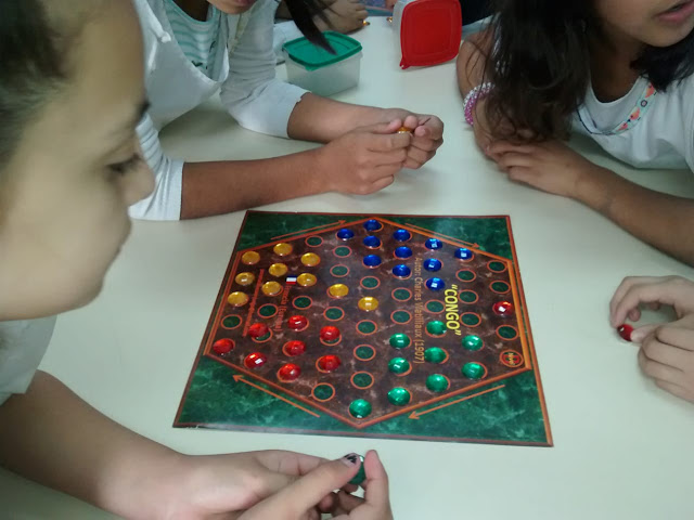 la imagen muestra alumnos frente al tablero de un juego en la mesa