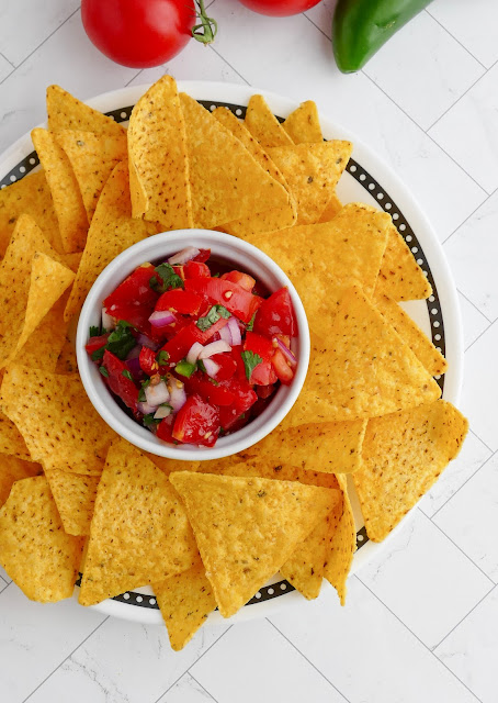a bowl of pico sitting on a plate surrounded by tortilla chips.