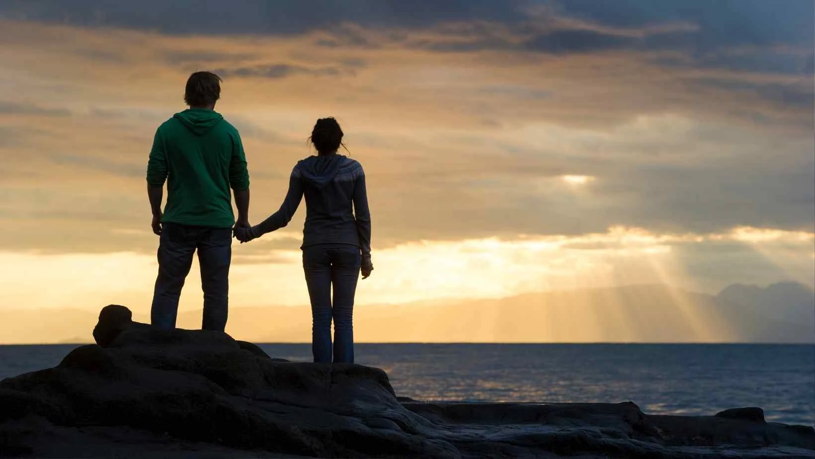 canva pro stock image of a couple holding hands and silhouetted against a sunrise