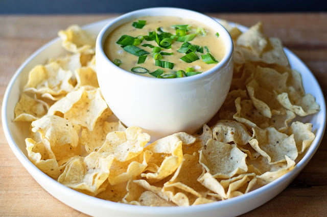 The queso, in a bowl, on a platter, with chips