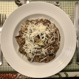 White plate containing risotto sprinkeld with grated cheese. Cutlery is visible at the edges of the picture.