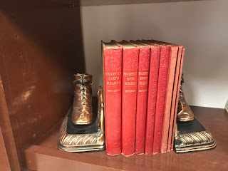 set of old red reading primers on a shelf