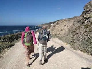 2 hikers on a road, left the sea, right a round military ruin
