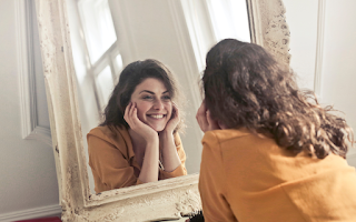 A confident woman looking at her positive self-reflection in the mirror, with affirmative words reinforcing her self-worth and inner beauty.