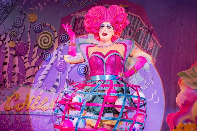 A dame with pink hair, pink gloves and a skirt full of balls on stage at Mercury Theatre Colchester