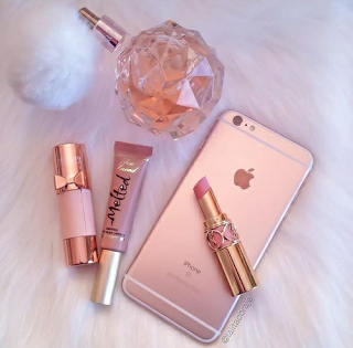 A flat lay photo with rose gold accessories, including perfume bottle, lipgloss, and rose gold iphone 7