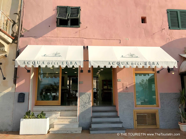 A pink house facade with green shutters and a boutique selling perfume on the ground floor.