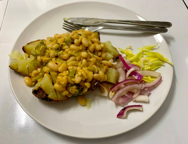 Curry beans on a jacket potato with pickled onion and celery leaves