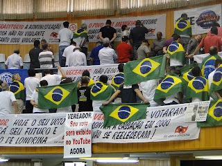 Foto: manifestantes nas galerias da câmara de vereadores, no dia da cassação do Prefeito Barbosa Neto. Todos de costas e cobertos com a bandeira do Brasil, para o prefeito que falava naquele momento. 