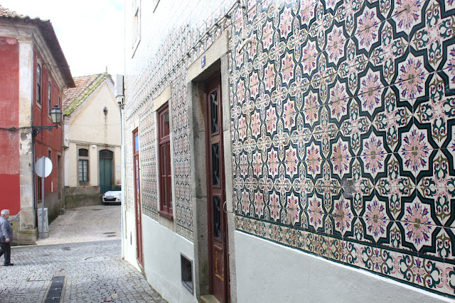 Jedna z uliczek w centrum Ovar. Wąska, brukowana ulica. Fasada stojącego przy niej domu dekorowana jest ceramicznymi płytkami okładzinowymi o stylizowanym, kwiataowym wzorze. 