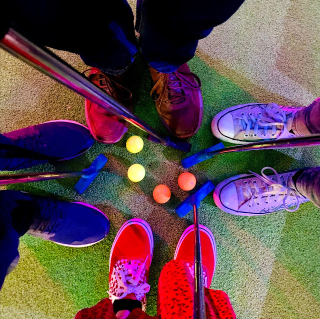 Four people's shoes surrounding golf balls and clubs