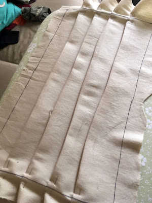 A beige rectangle of fabric with the edges marked with black sharpie and large seam allowances left outside the marks, with four very wobbly inch-deep pleats pressed into it. A single silver pin holds each end of each pleat down.