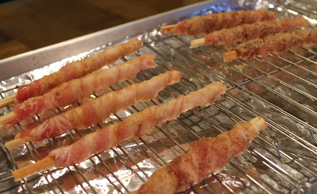 Bacon-wrapped breadsticks on a rack ready to bake in the oven.