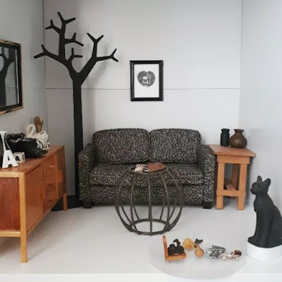 Collection of one-twelfth scale modern miniatures in a cubby, including a sideboard, large 2-dimensional tree, sofa, side table large Egyptian cat sculpture and coffee table in front of the sofa.