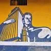 A mural of a man holding a building in front of a yellow and blue building.