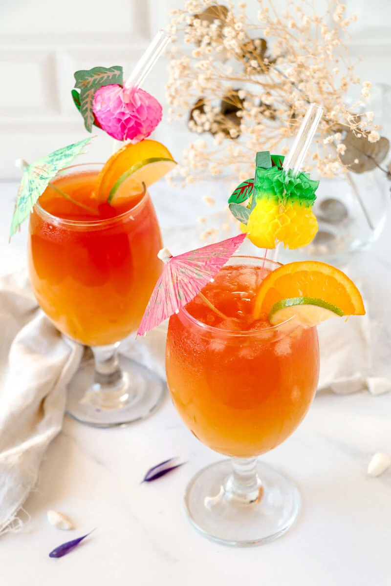 Two glasses of rum punch with umbrellas and citrus slices.