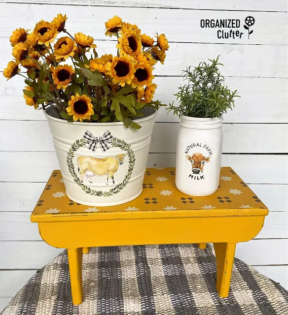 Photo of a painted and stenciled farmhouse bench, with upcycled bucket & jar.