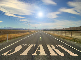 A road, beginning at the bottom of the image and stretching away from the viewer into the background, fading in the distance. In the foreground, the word 'start' is stenciled on the road in large white letters.