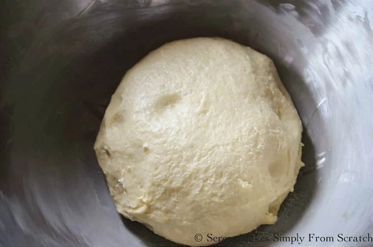 Hawaiian Roll Dough in a ball placed in a buttered stainless steel bowl.