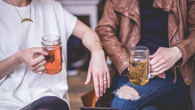 two people sitting next to each other holding cups of tea