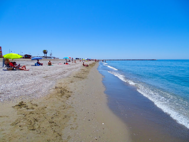 Orilla de playa bañada por las azules aguas del mar y el cielo azul de fondo