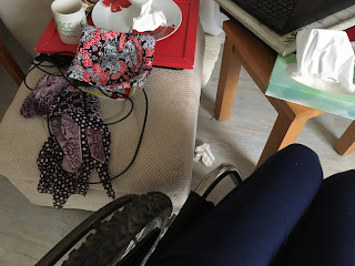 photo from wheelchair users perspective of their lap next to some crockery, tissues, scarf, charger on a cushion..