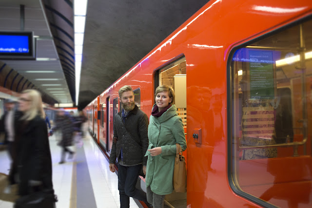 Nainen ja mies astuvat ulos metrosta. Taustalla muita matkustajia.