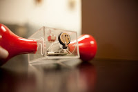 To demonstrate the supercapacitor's ability to store power, the researchers modified an off-the-shelf hand-crank flashlight (the red parts at each side) by cutting it in half and installing a small supercapacitor in the center, in a conventional button battery case, seen at top. When the crank is turned to provide power to the flashlight, the light continues to glow long after the cranking stops, thanks to the stored energy. (Photo Credit:  Melanie Gonick) Click to Enlarge.