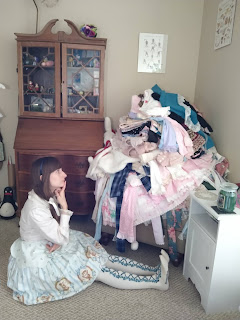 A lolita sitting on the ground and looking troubled at a big pile of clothes.