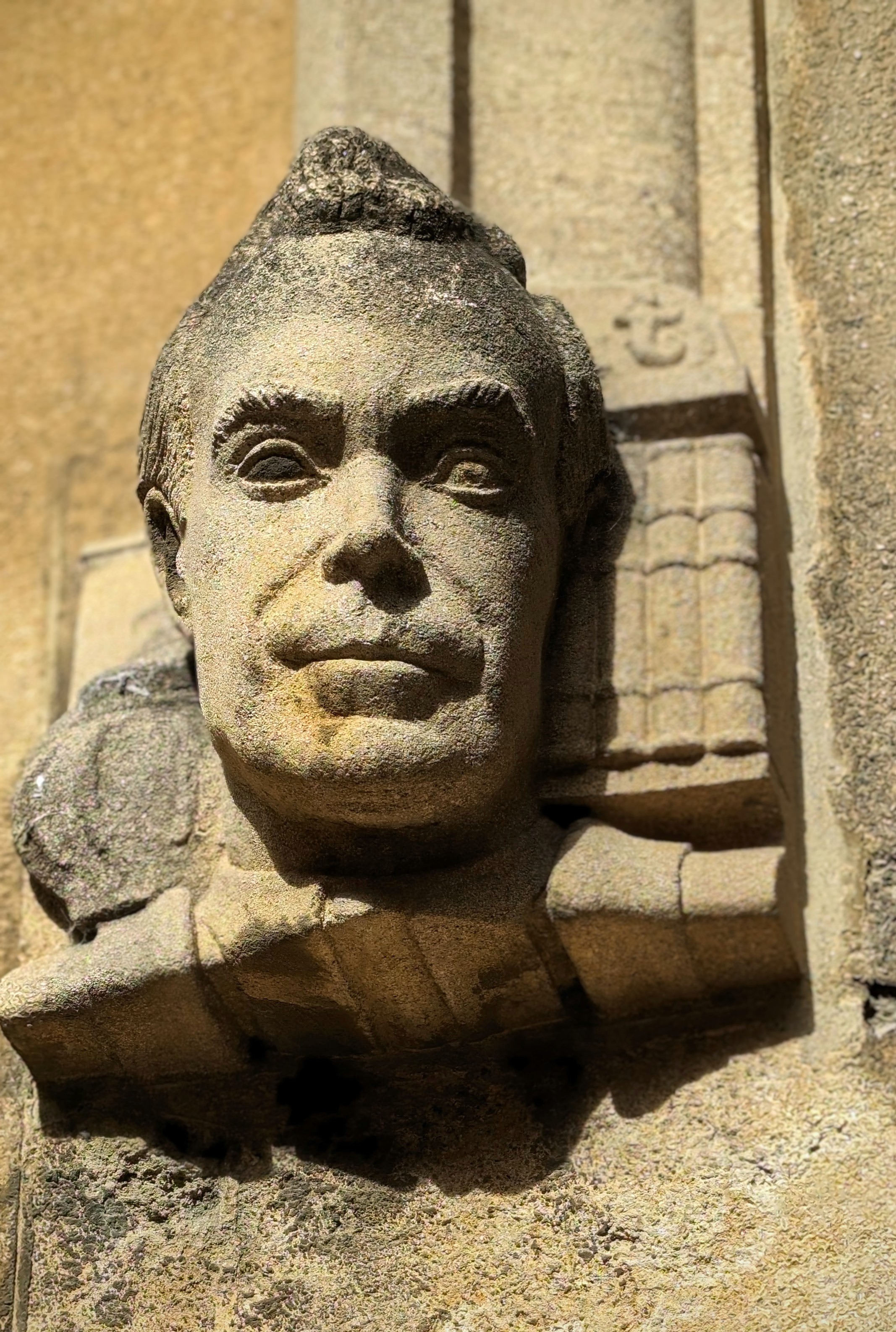 Stone caved head and shoulders high on a stone wall. It looks a lot like Robbie Williams, but it can't be as it's in the Bodleian Old Library.