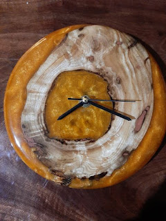 A round clock face with no numbers, made from a piece of black walnut wood and tiger orange resin.