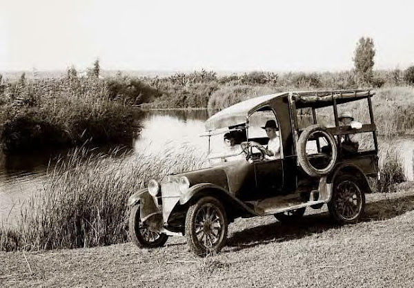 Man & family in old car by river