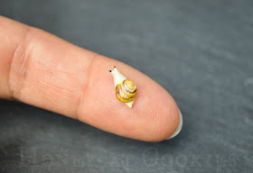 Close up of very tiny royal icing snail on human finger for scale