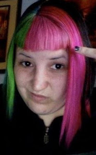 Photo of Lara from 2011, a pale skinned person looking at the camera with a smirk on her face. She has split neon green, neon pink hair (dyed with Special Effects Atomic Pink) with a short fringe.