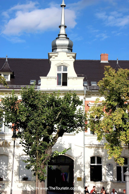 People sitting in an alfresco cafe in front of a bright white period property under a blue sky.