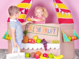 A girl sells fruits to a boy, engaging in pretend play as they enact a supermarket scene.