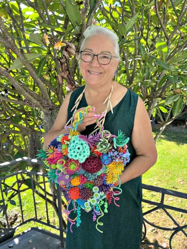 smiling woman holding heart-shaped colorful quilled display that depicts sea vegetation