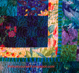 Detail of border of a Radiant Nine-Patch quilt. Three borders: a pink-backroung floral, a blue and green stripe and a large pieced outer border of blue, green and purple.