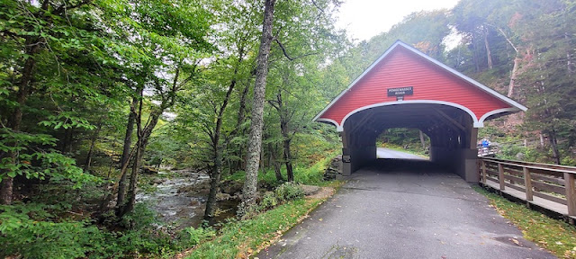 Bright red covered bridge on right. Rocky brook in the tree on left.