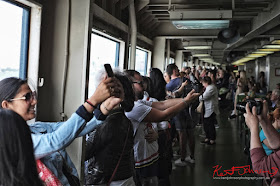 Tourists line the railings of a Staten Island Ferry and take selfies as it passes the Statue of Liberty. Travel photography by Kent Johnson.