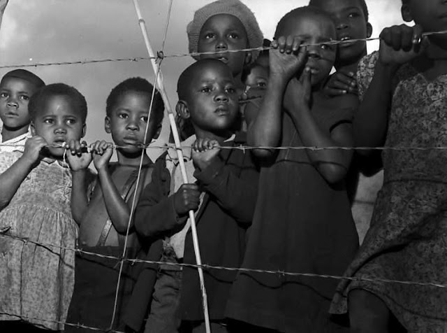 Crianças atras de uma cerca de arame farpado durante o apartheid em 1950 na Africa do Sul