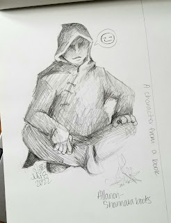A photograph of a pencil sketch in a sketchbook. The drawing is a hooded and cloaked figure sitting cross-legged in front of a small fire. The figure's face is shaded and his mouth is smirking slightly.