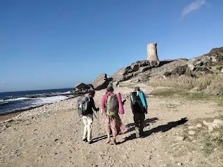 4 hikers walking along a beach, in the background a round old tower