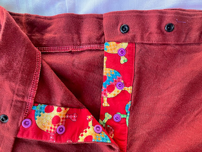 a close up of the placket and the snaps used to close it. The placket fabric is bright red with large skulls on it. The snaps are lavender. End ID.