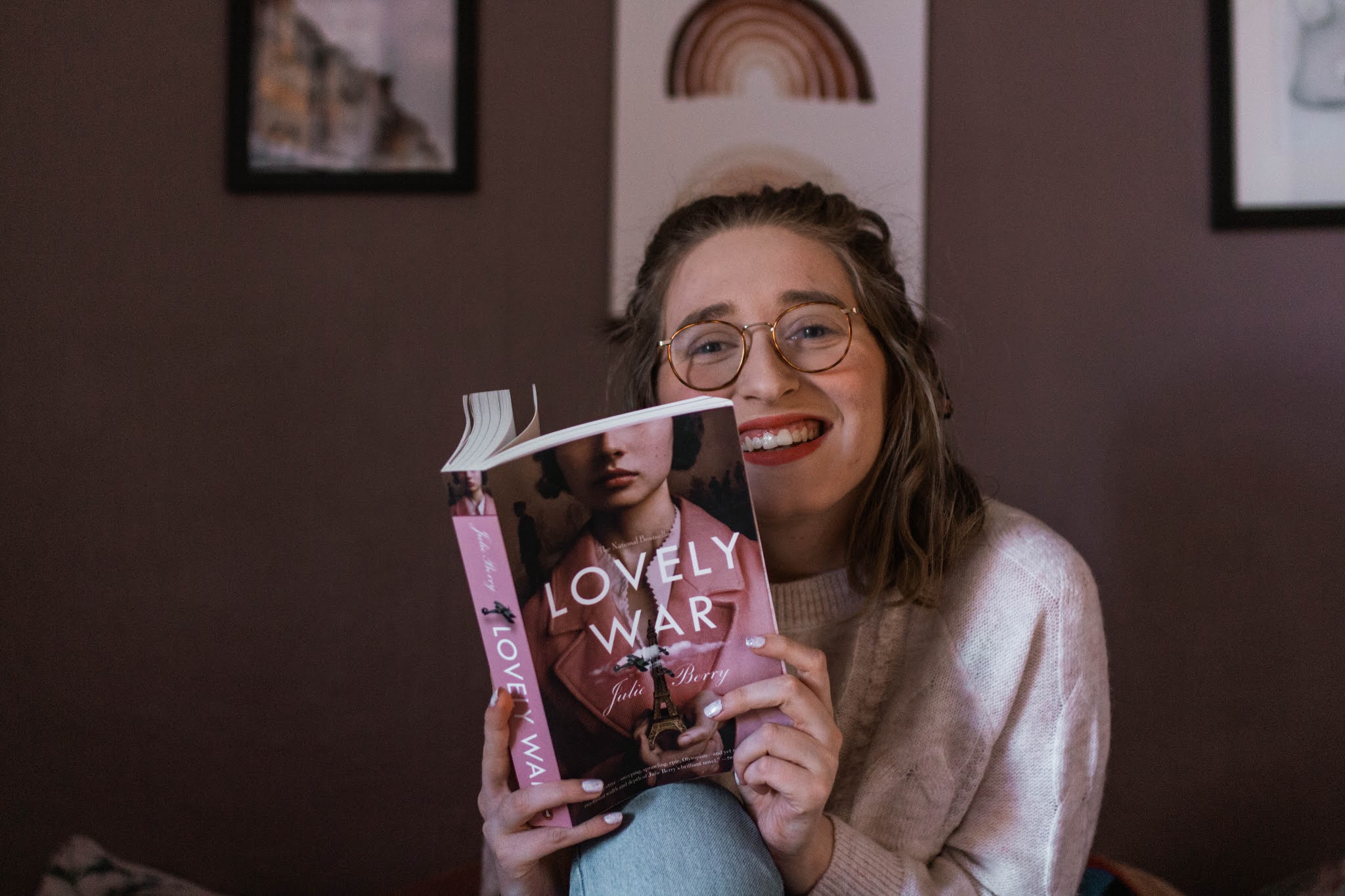 girl smiling while reading a pink book lovely war by julie berry