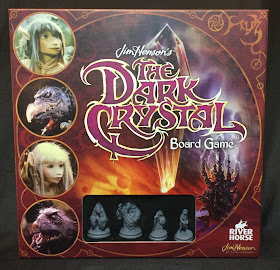 The cover of the game. The title is displayed superimposed over the titular crystal, with the castle of the crystal visible in the background. Along the left side are the four main characters, each in a circular portrait. Along the bottom is a window covered with clear plastic allowing the four miniatures that are the game's playing pieces to be seen.